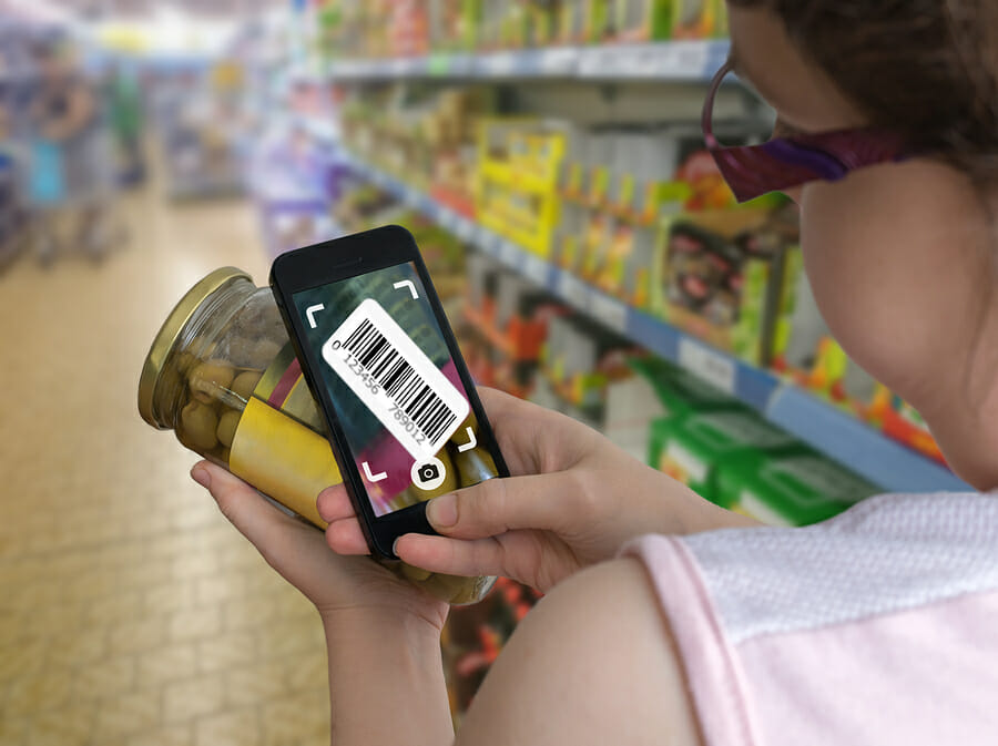 Woman is shopping in supermarket and scanning barcode with smartphone in grocery store to get online info about product.