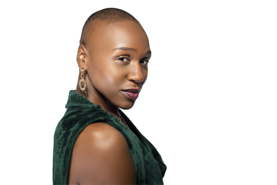 Beautiful black African American female model posing confidently with bald hairstyle on a white background.  The woman is portraying uniqueness and individuality.